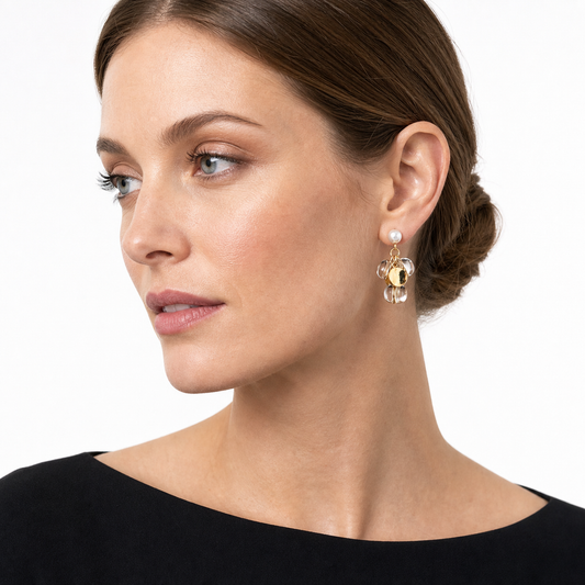 Side-profile studio portrait showing a white pearl stud and compact gold-and-clear statement drop earring.