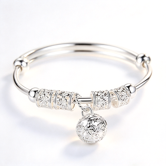 Angled view of a bell charm bangle bracelet showing its curved band, decorative center details, and hanging round charm