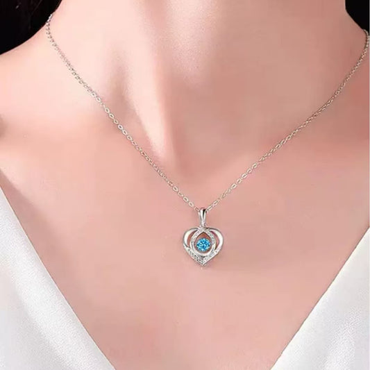 Blue heart pendant necklace worn at the neckline, showing the small heart-shaped design against a white top.