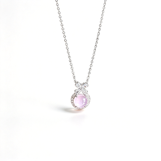 Pendant necklace with a pink round centerpiece, bow detail, and fine chain shown against a light background.