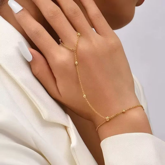 Close-up of a gold-tone hand chain bracelet extending from a finger ring area to the wrist with small bead details.