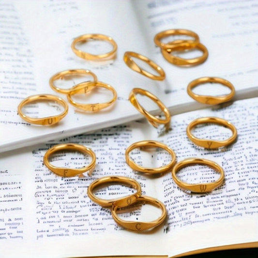 Gold-tone initial rings displayed across an open book, showing different letter designs.