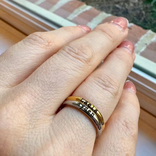 Close-up of a personalized name ring worn on a finger, showing layered bands in gold and silver tones