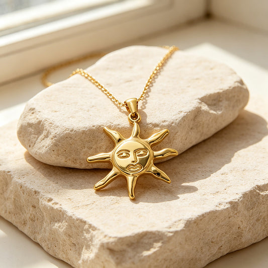 Sun-shaped face pendant and chain arranged on a textured beige stone surface