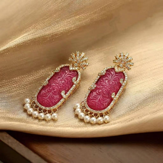 Close-up of the vibrant magenta gemstone earrings with ornate gold carvings.
