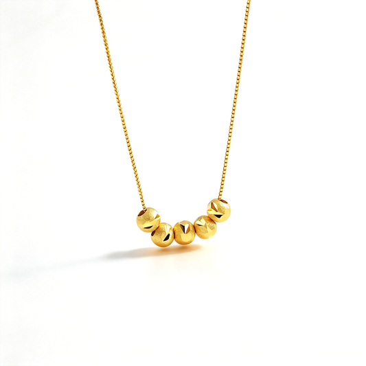 Gold-tone geometric bead necklace displayed on white, showing the curved row of faceted decorative beads.