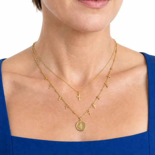 Model wearing the gold-tone cross-charm and beaded starburst necklace in an opposing three-quarter pose