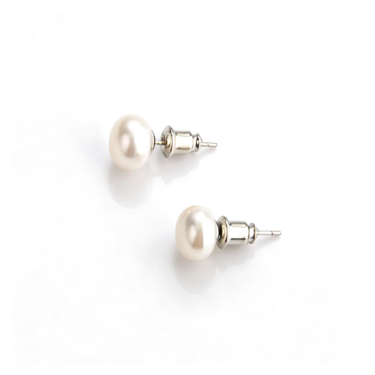 Angled view of shiny natural white pearl stud earrings resting on a smooth reflective background.