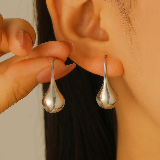 Close-up of gold-tone teardrop dangle earrings worn on an ear, showing their smooth, elongated shape.