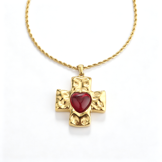 Front perspective of a chunky gold-plated Byzantine cross pendant with a red heart-shaped gemstone.