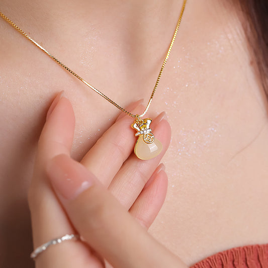 Close-up of the money bag pendant necklace worn at the neckline, showing its small decorative charm.