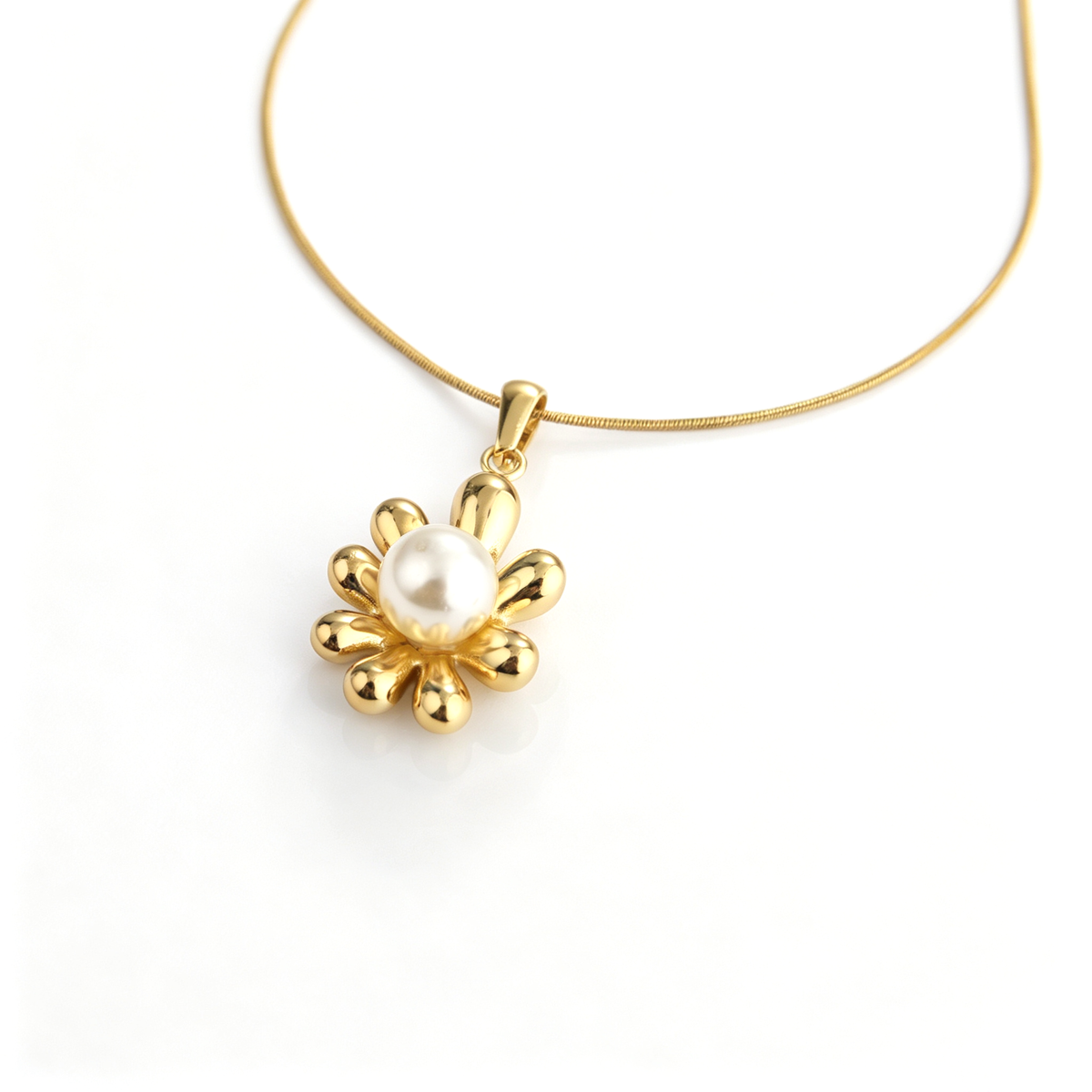 Angled close-up of a gold-plated flower pendant centered with a white pearl on a snake chain.