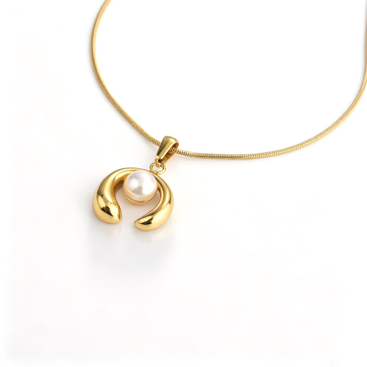 Angled close-up of a gold-plated curved arch pendant with a central pearl on a snake chain.