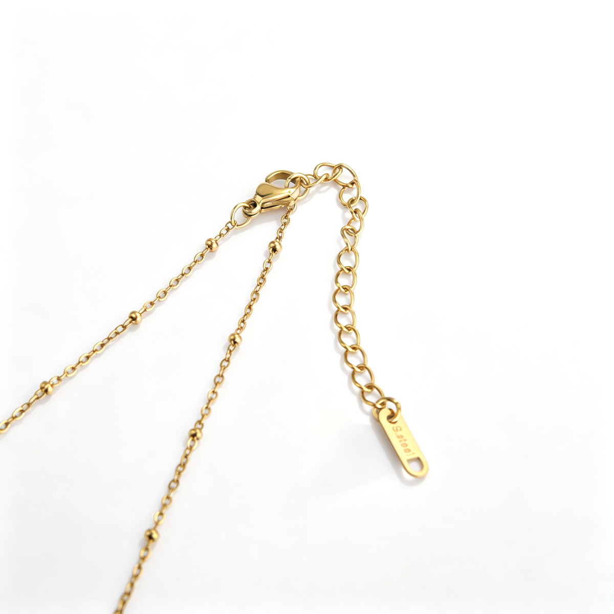 Close-up of the gold-plated lobster clasp, extension links, and logo tag on a beaded chain.