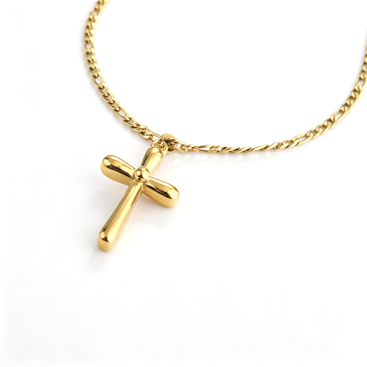 Angled view of a polished 18k gold plated puffy cross pendant attached to a classic Figaro chain.