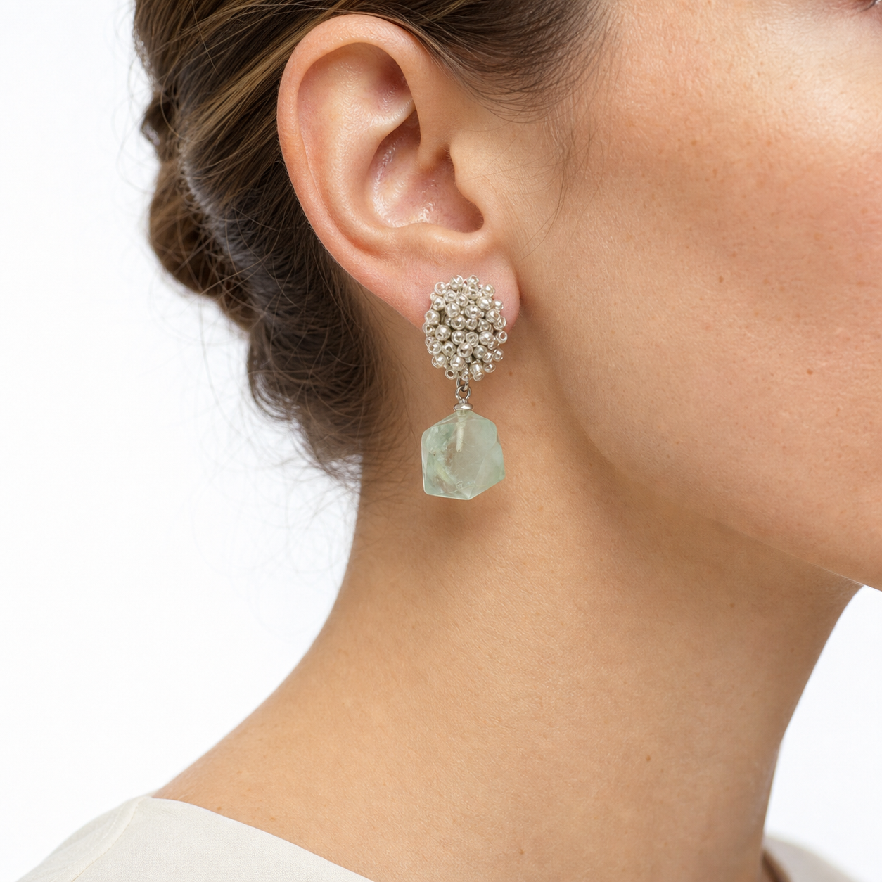 Close-up of an ear wearing a silver beaded-top green aventurine drop earring, showing the post, connector, and pale faceted stone.