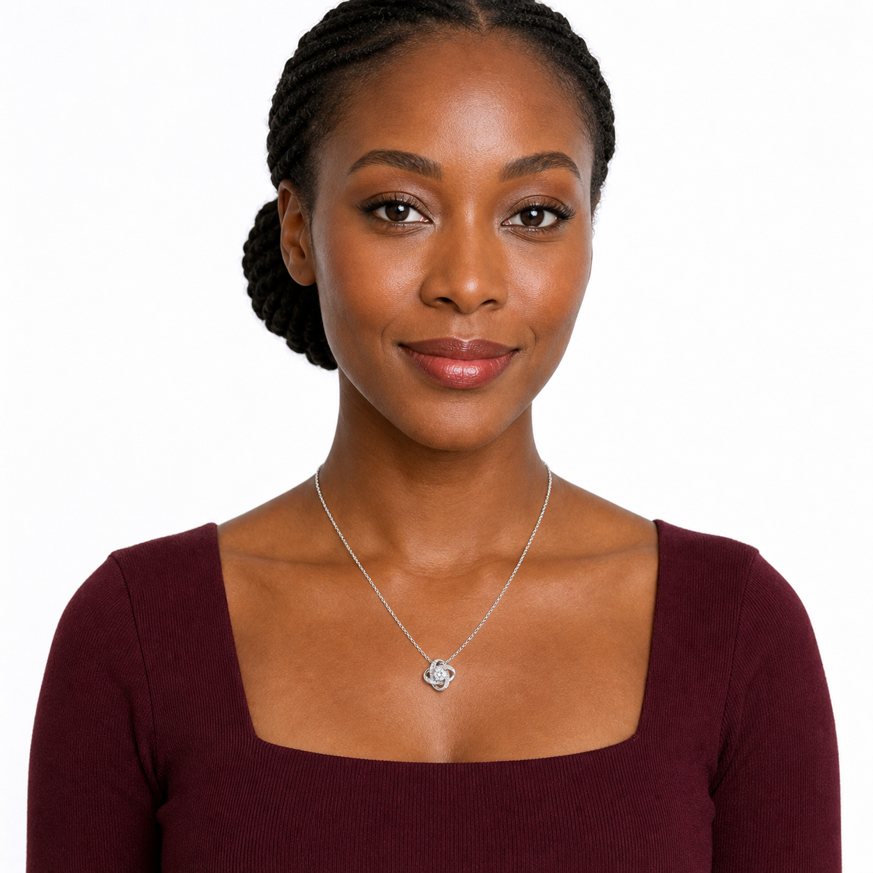 Black woman wearing a silver-tone love knot CZ pendant necklace with a burgundy square-neck dress in a white studio.