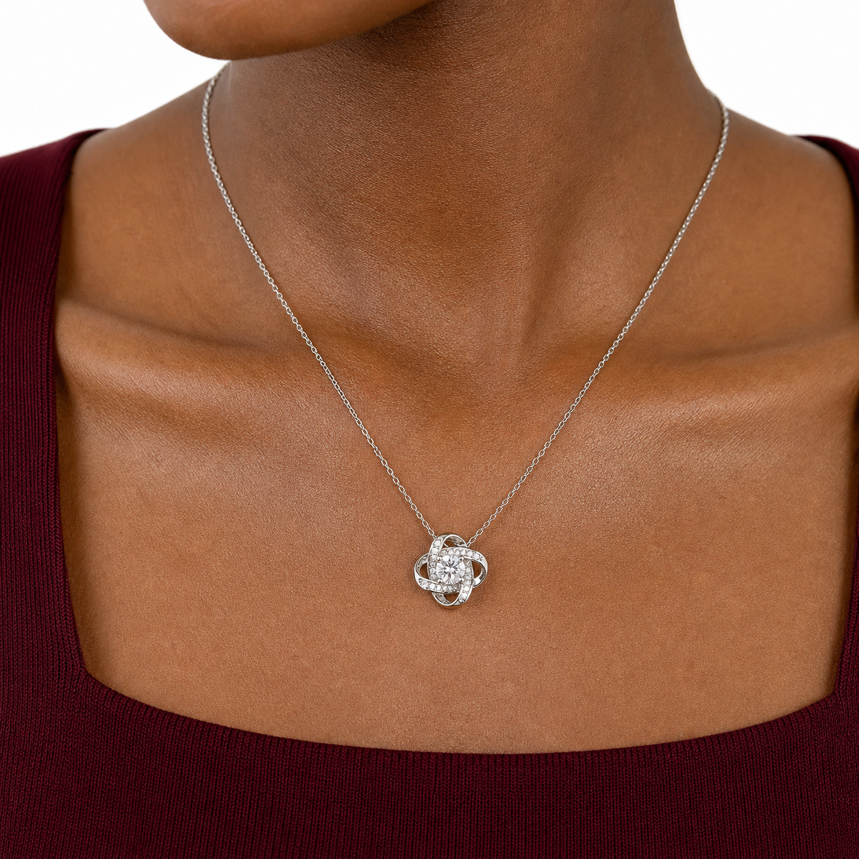 Close-up of a silver-tone love knot pendant with a round CZ center and pavé details on a fine chain.