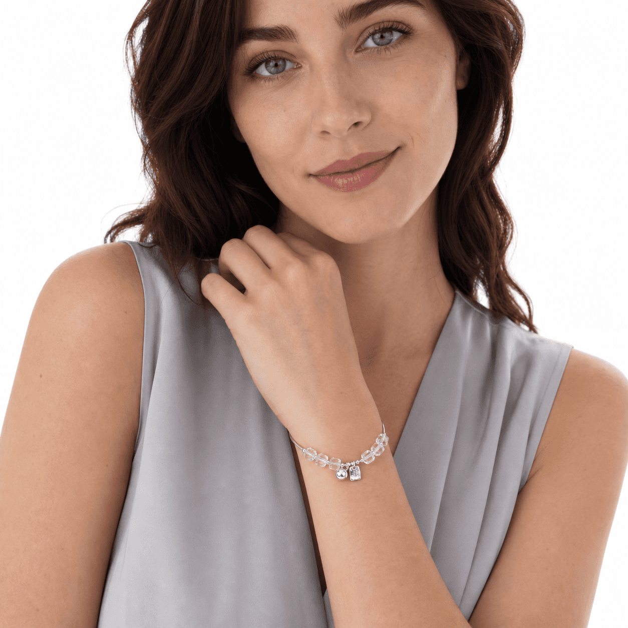 Woman wearing a clear crystal adjustable bracelet with faceted cube beads and two silver-tone charms on a white studio background.