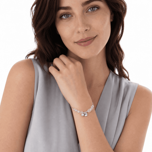 Woman wearing a clear crystal adjustable bracelet with faceted cube beads and two silver-tone charms on a white studio background.