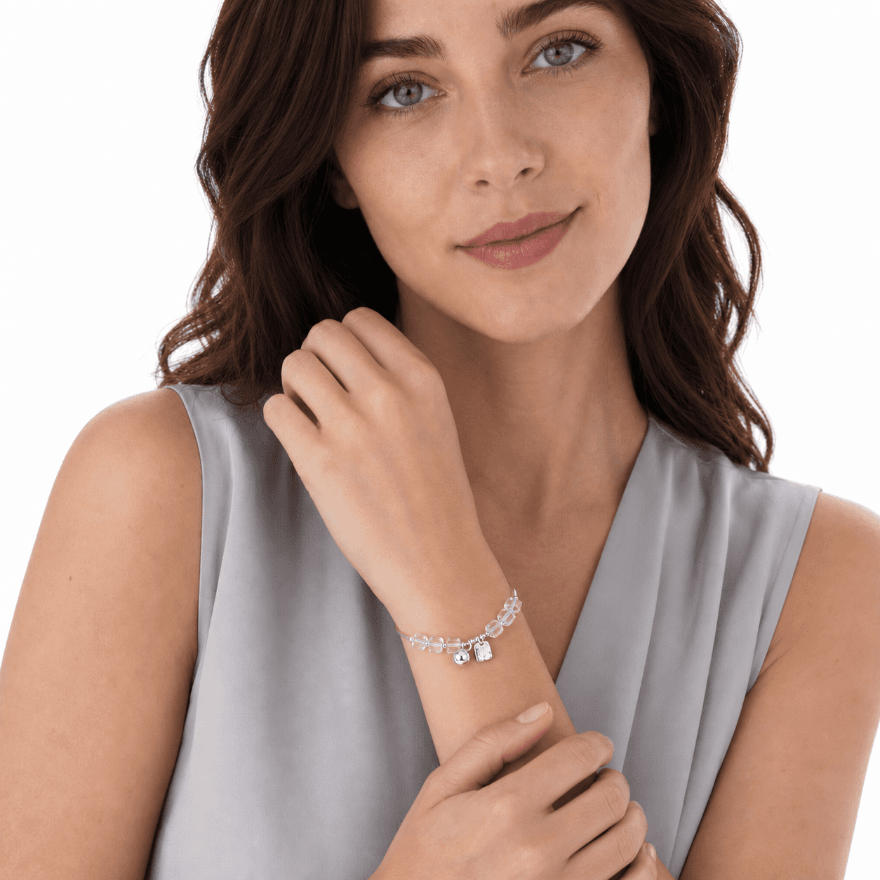 Front portrait of a woman showing a clear beaded bracelet with silver-tone tubes and dangling sphere and tag charms.