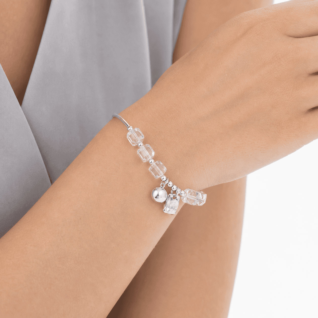 Close-up of a woman's wrist wearing a 17 cm clear crystal bracelet with faceted cube beads and silver-tone charms.
