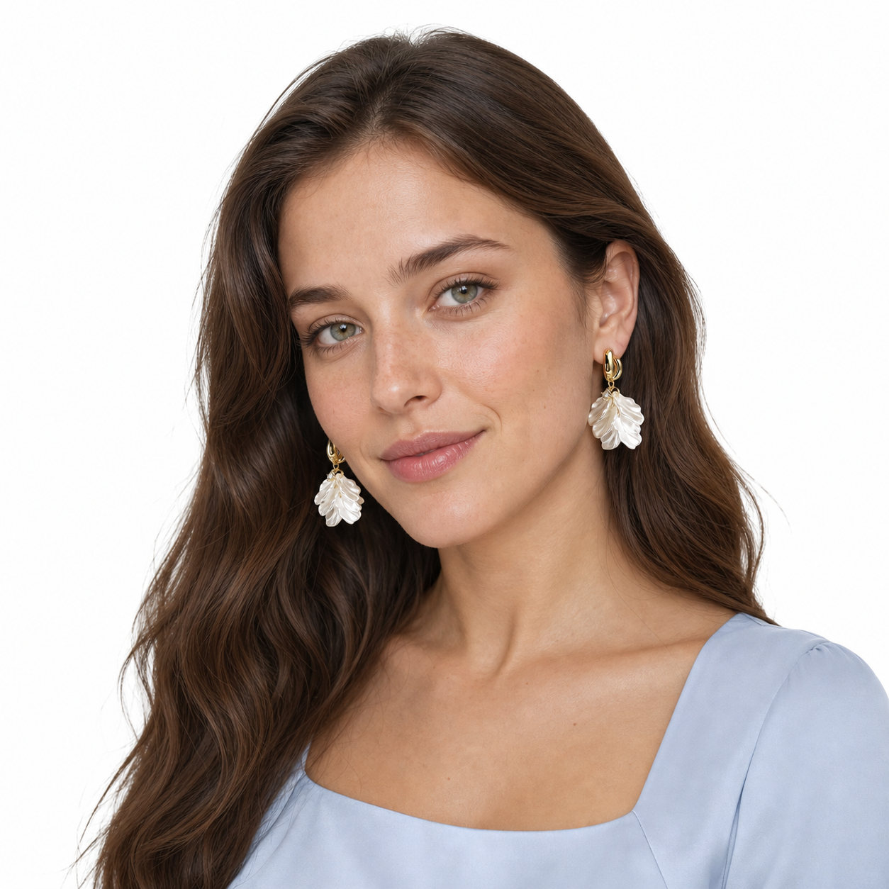 Young long-haired woman in a three-quarter white-studio portrait wearing gold double-hoop earrings with pearlescent floral petal drops.