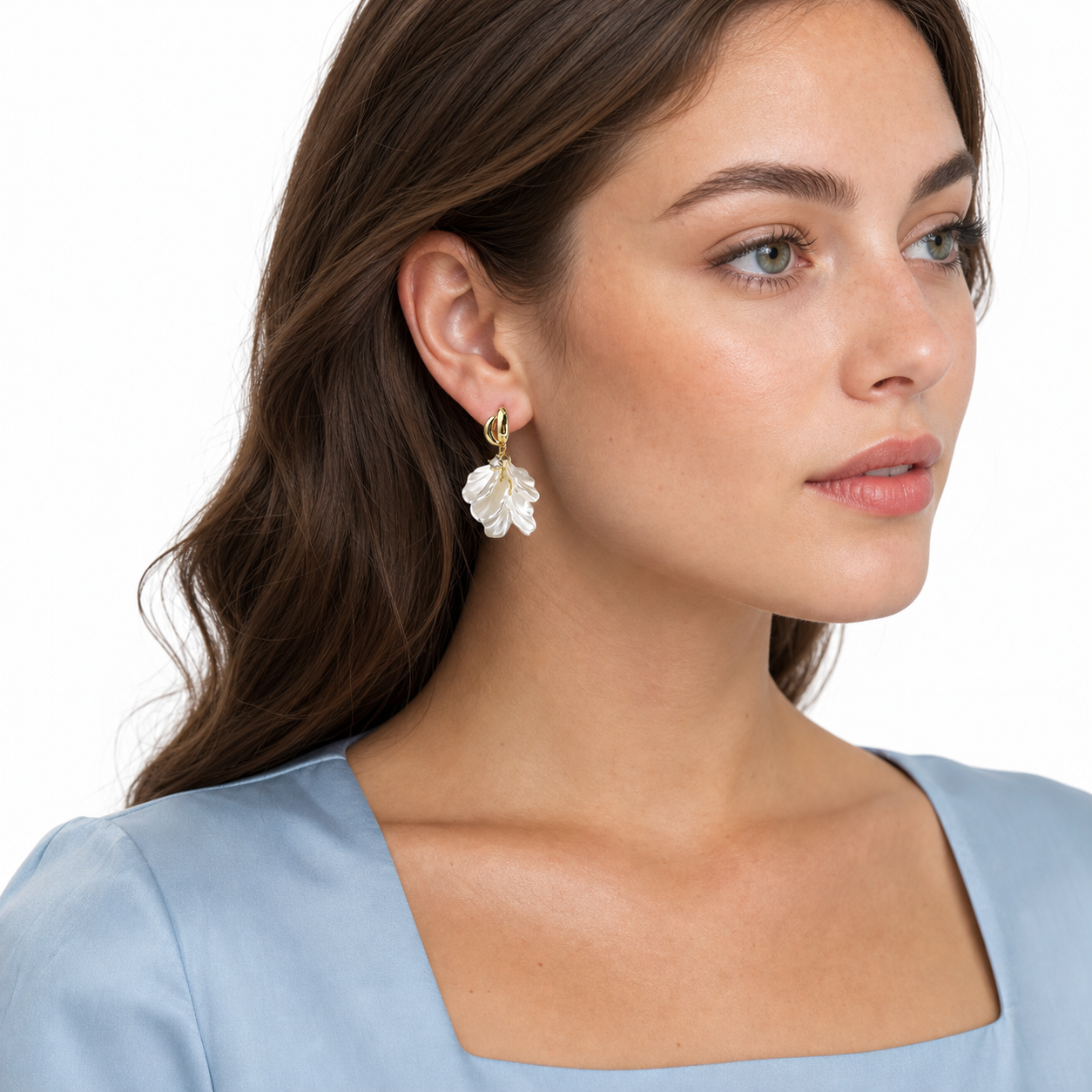 Side-profile portrait of a long-haired woman wearing floral hoop earrings with two gold oval loops and translucent ivory petals.