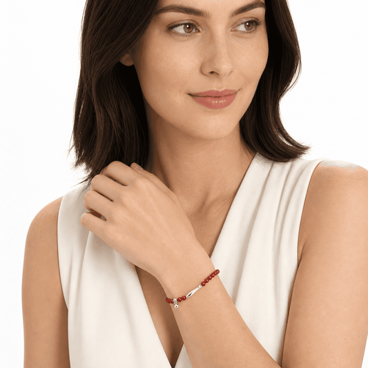 Woman in an ivory top wearing a koi red agate stretch bracelet on her raised left wrist in a white studio