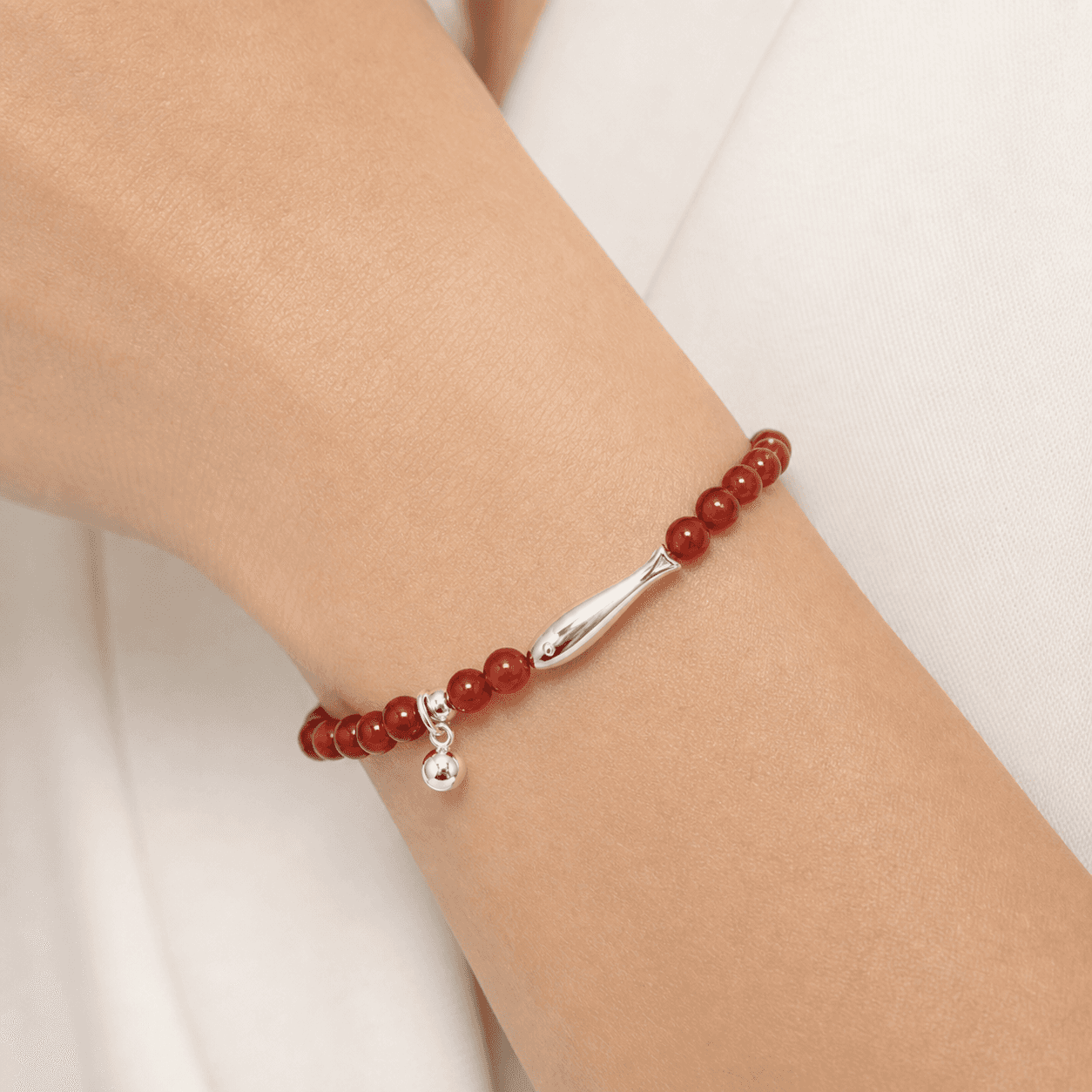 Macro wrist view of the translucent red agate bracelet with its silver-tone koi centerpiece and single sphere charm.