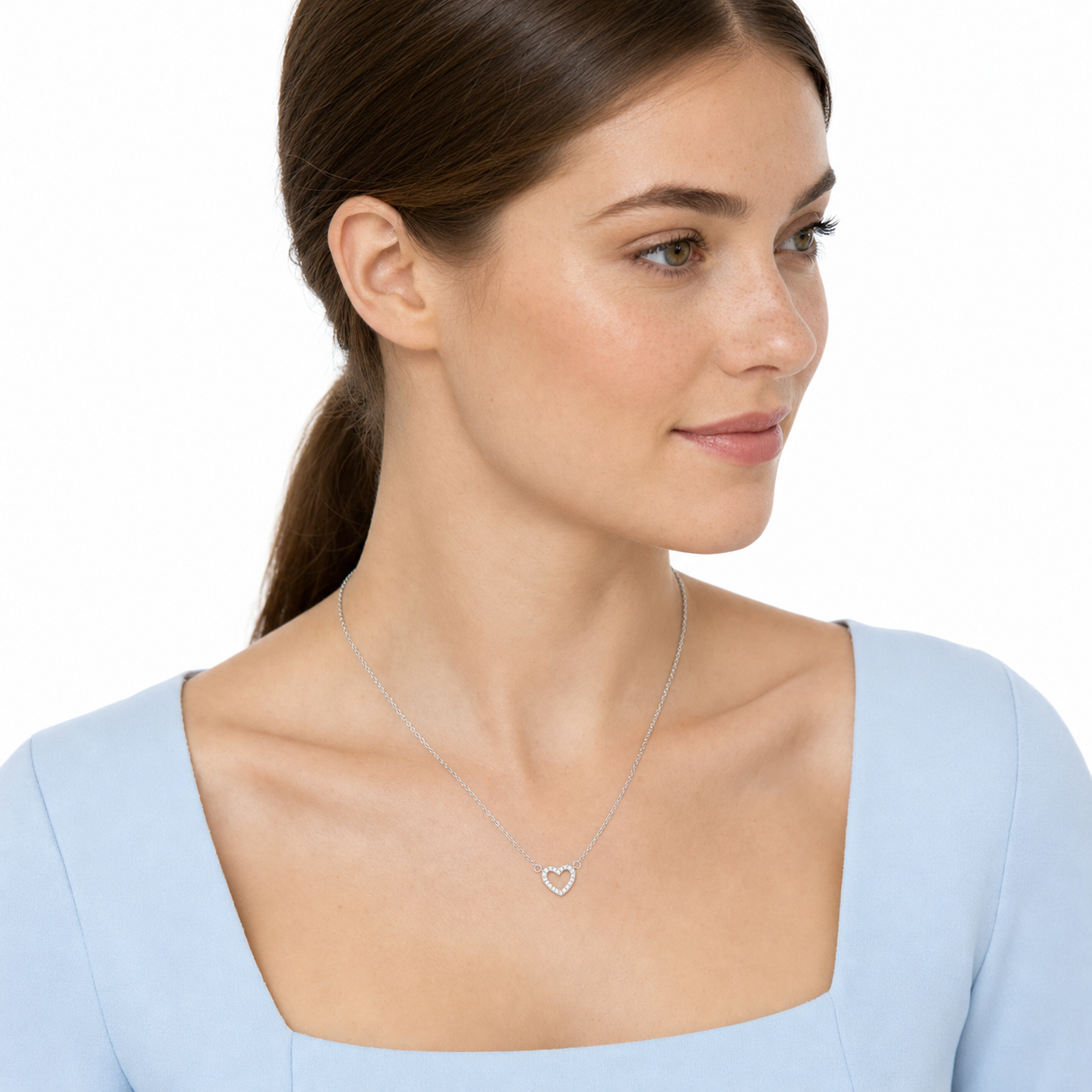 Three-quarter portrait of a young woman wearing a delicate silver-tone CZ open heart necklace.