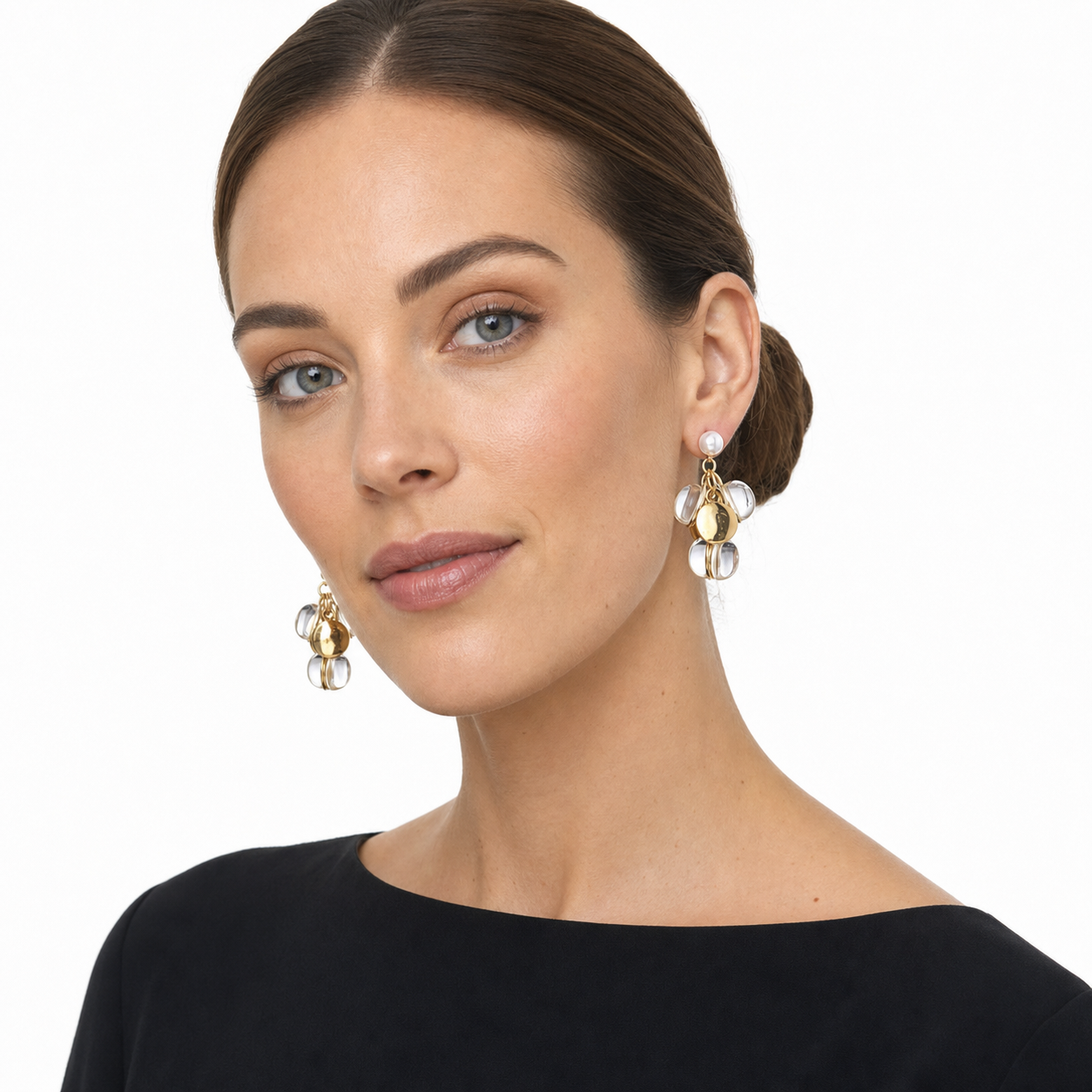 Western woman in a three-quarter white-studio portrait wearing pearl drop earrings with gold and clear clustered discs.