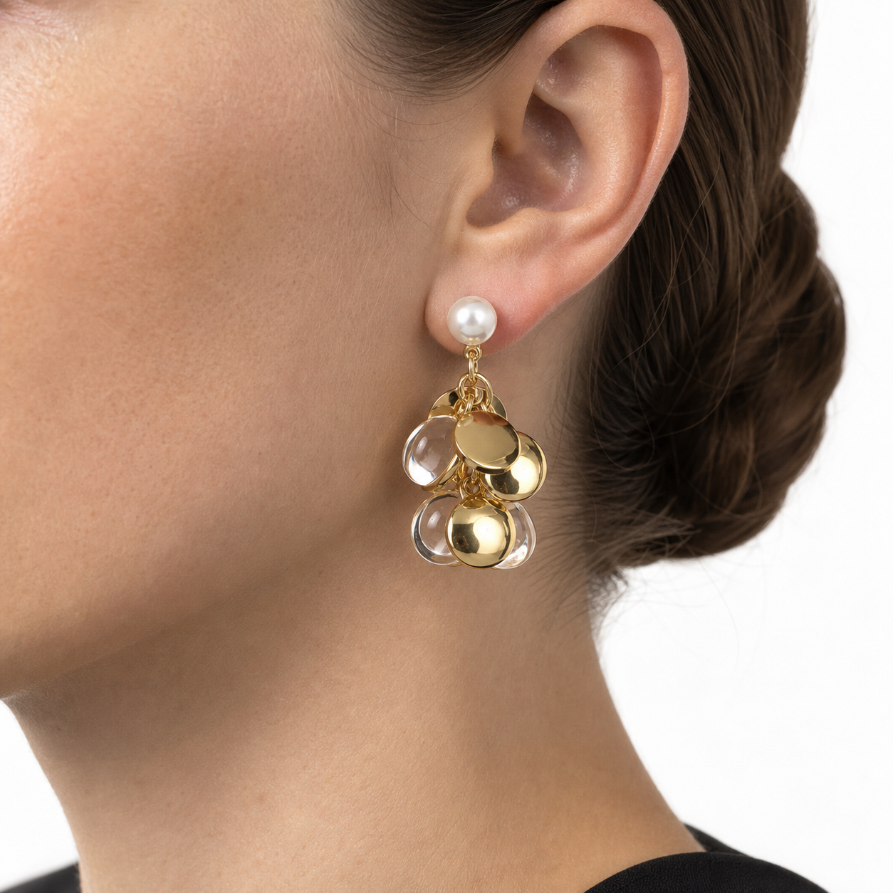 Close-up of an ear wearing a pearl drop earring with articulated gold and transparent round cluster charms.