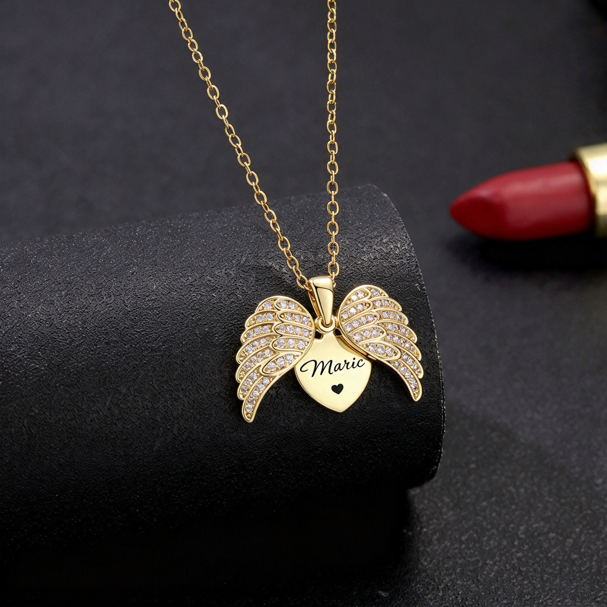 Gold-tone angel wings necklace displayed against a dark background, highlighting the heart pendant.