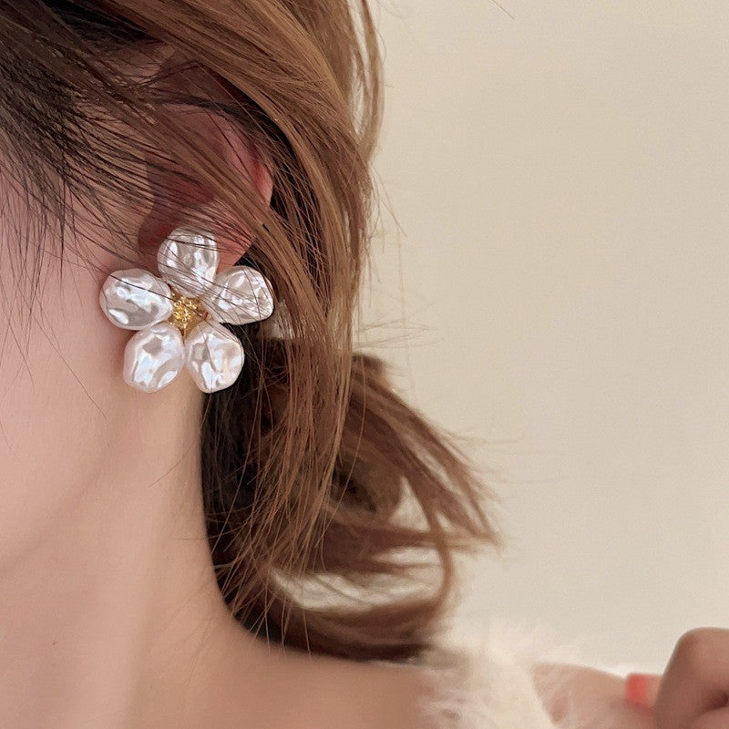 A flower stud earring with irregular white petals shown worn on an ear in a close-up lifestyle photo.