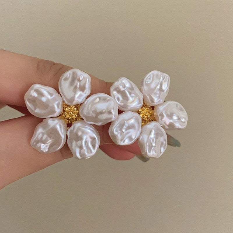 Two matching flower stud earrings held in a hand, showing the dimensional petals and textured centers.