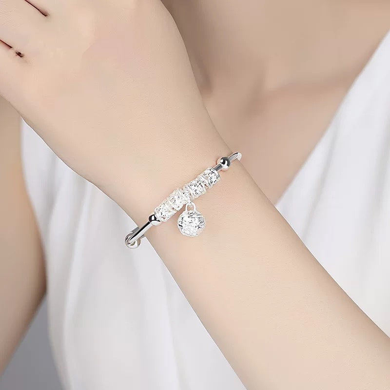 Bell charm bangle bracelet worn on the wrist, showing the delicate dangling charm and decorative center design