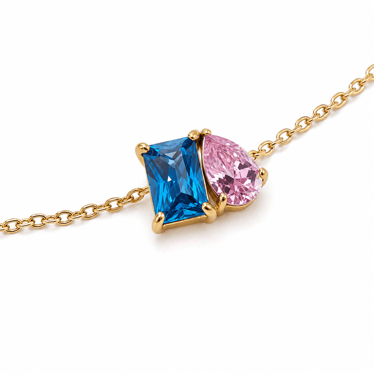 Low-angle close-up of blue rectangular and pink pear-cut zircon stones in gold prong settings