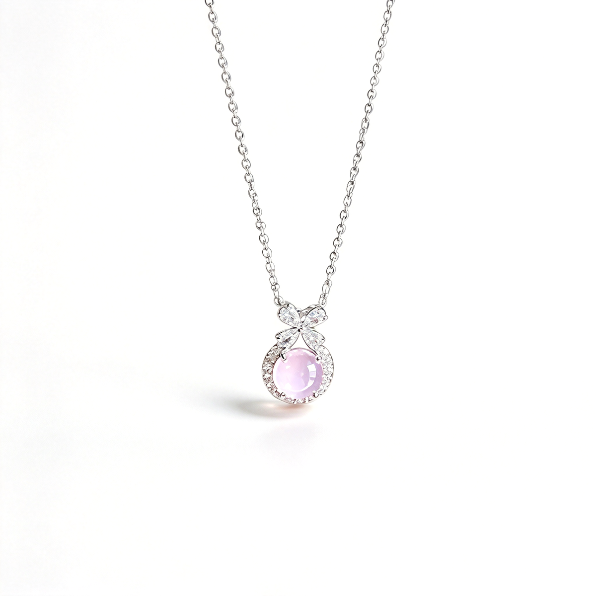 Pendant necklace with a pink round centerpiece, bow detail, and fine chain shown against a light background.