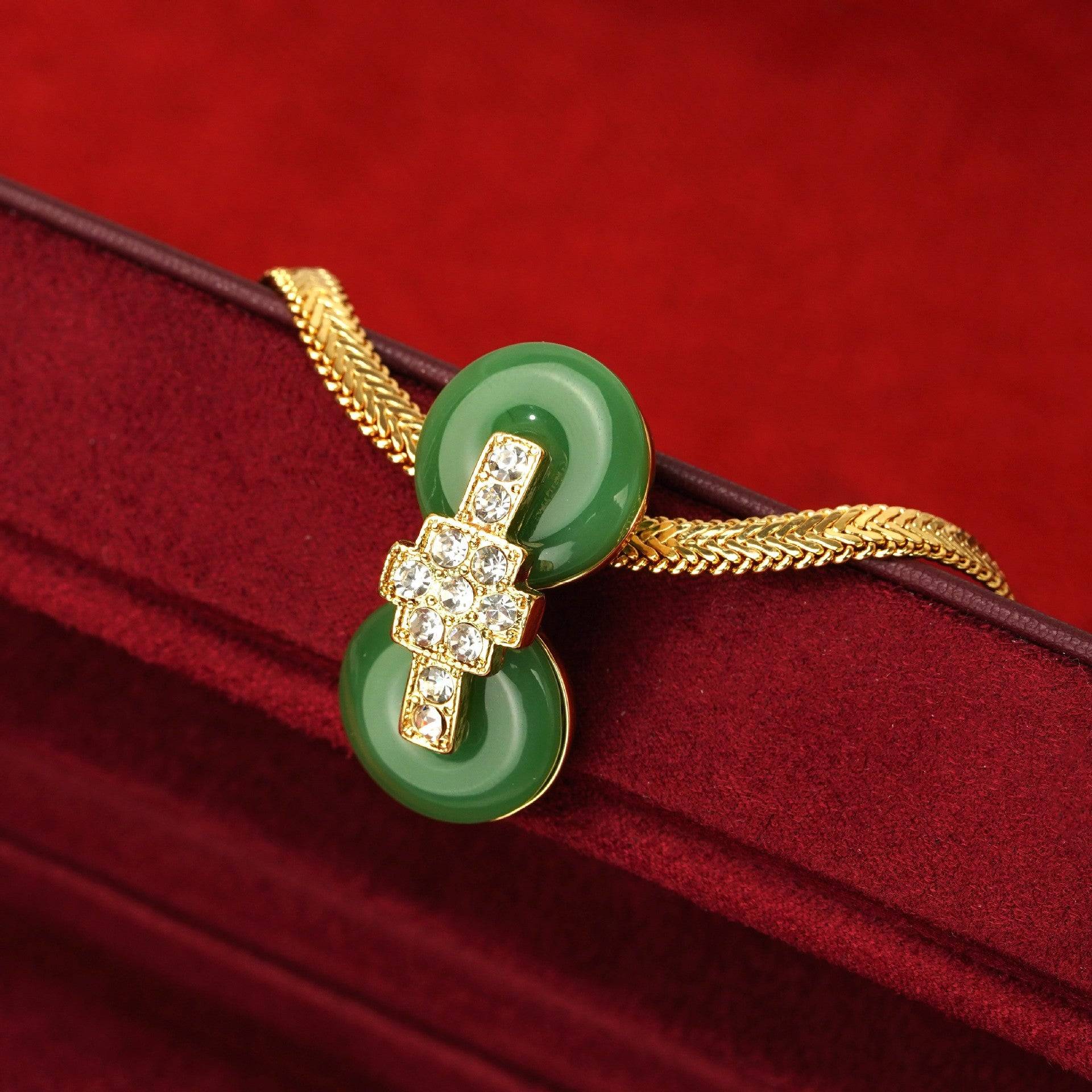 Profile close-up of Ever P. luxury real gold-plated geometric cross green crystal pendant resting on a dark velvet display case.
