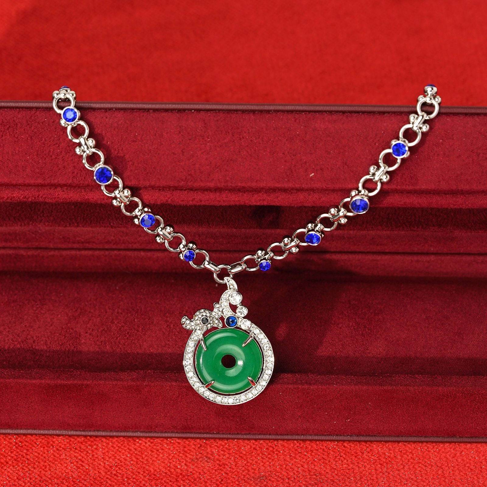 Front view of Chinoiserie vintage green crystal donut necklace showcasing the translucent green stone contrasted against rich sapphire blue link chain accents.