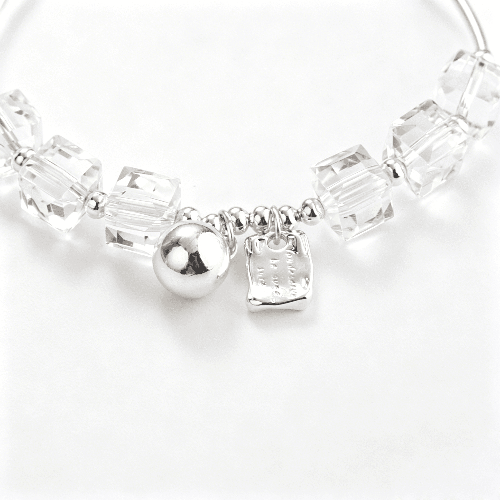 Close-up of clear faceted cube beads beside a silver-tone sphere charm and irregular rectangular tag charm.