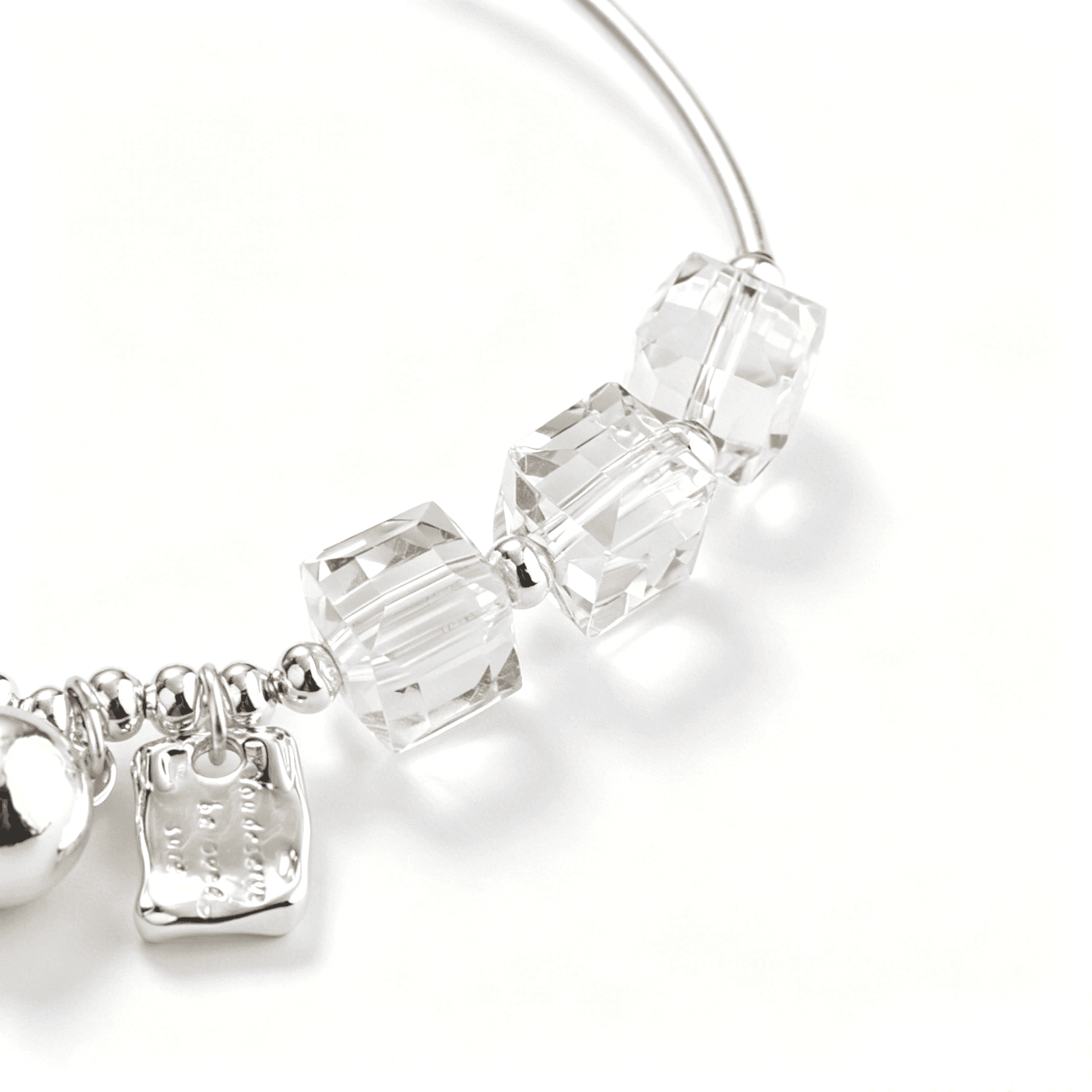 Macro view of transparent cube beads, polished round spacers, and silver-tone plated bracelet details.