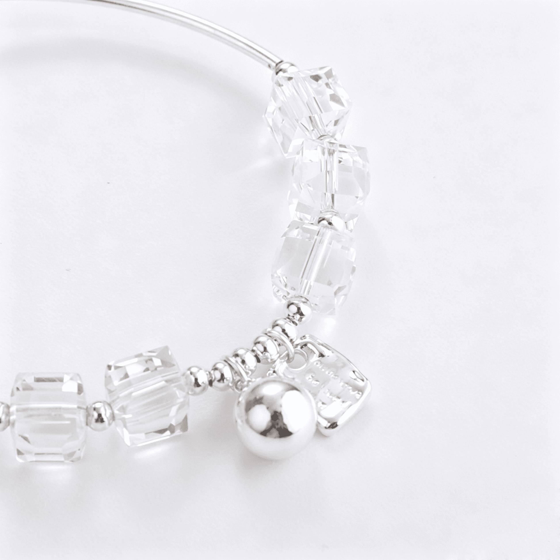 Angled detail of a clear crystal beaded bracelet with a curved silver-tone tube and two polished dangle charms.