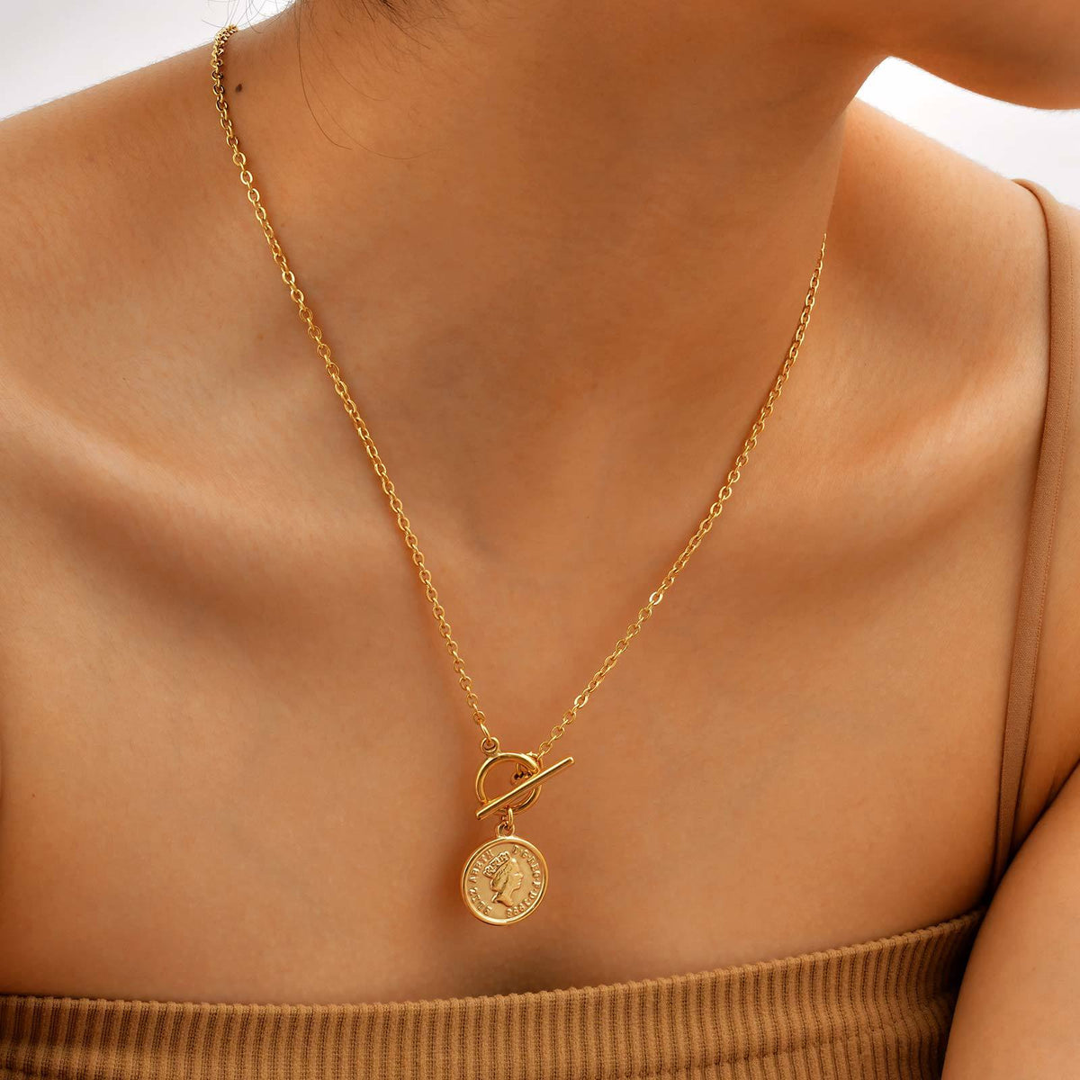 Side view of the coin pendant toggle necklace worn at the neckline with the charm resting near the collarbone.