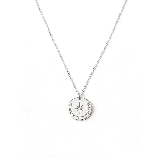 Silver-tone round pendant with a central compass star and directional lettering.