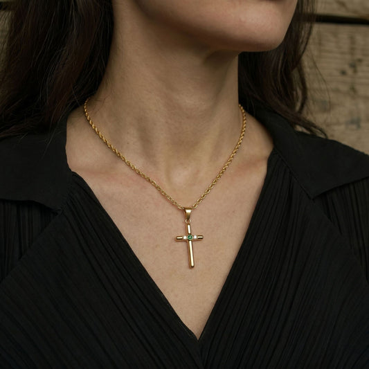 Close-up of a cross pendant necklace worn over a black V-neck blouse, showing the pendant resting at the neckline.