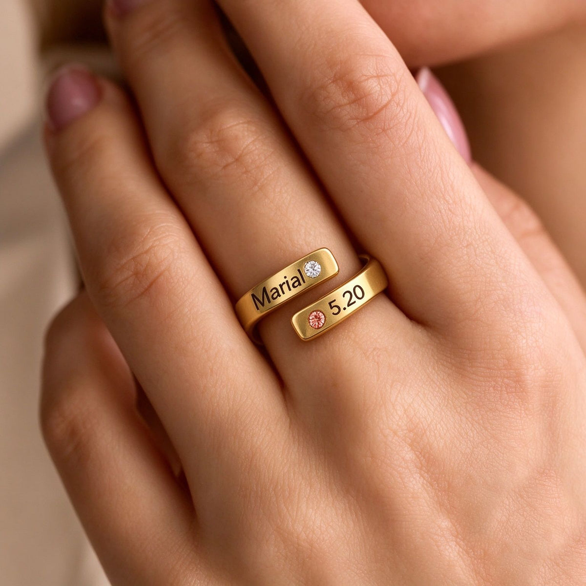 Close-up of a gold-tone open wrap ring with engraved name details and two decorative accents worn on a hand.