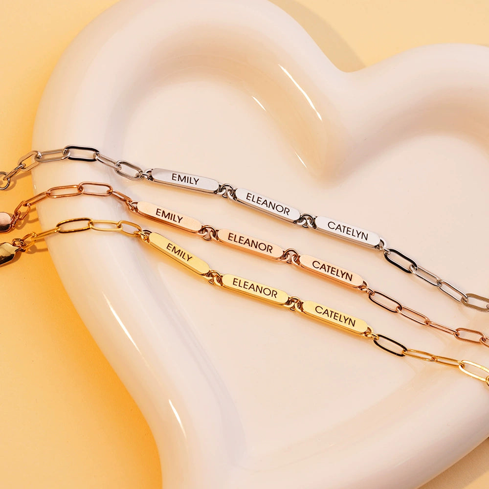 Close-up of the linked name bar bracelet arranged on a warm peach background, showing the chain and engraved bars.
