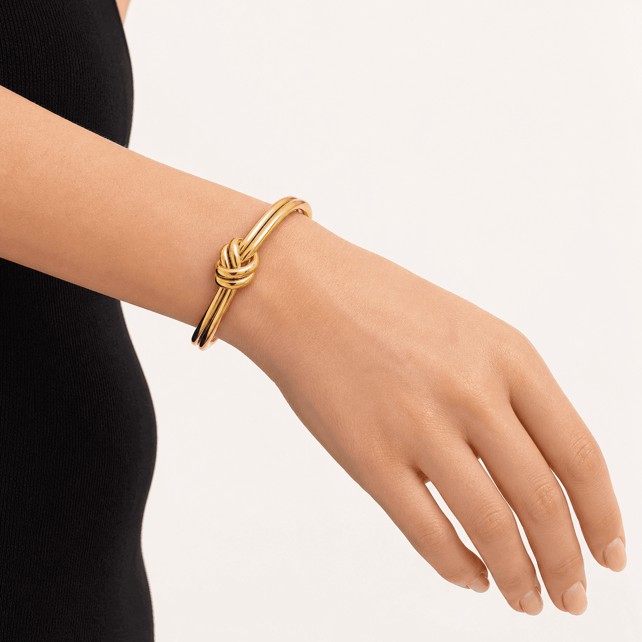 Close-up of a 14K gold-plated knot cuff bracelet wrapped around a woman’s wrist